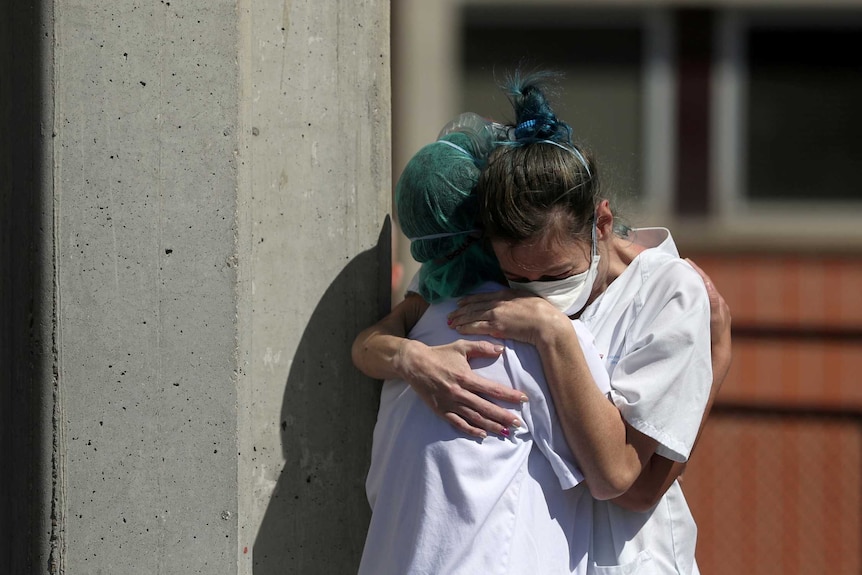 Medical workers hug each other while wearing face masks and hair nets