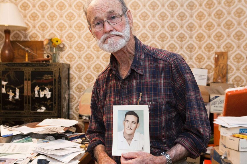 Avon Hudson, in a living room, holds a photo of a young man.