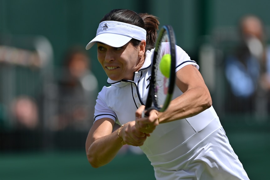 Australian Ajla Tomljanovic grimaces as she leans forward to hit a double-handed backhand at Wimbledon.