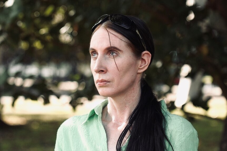 A woman in a green shirt with a dark ponytail stares into the distance.