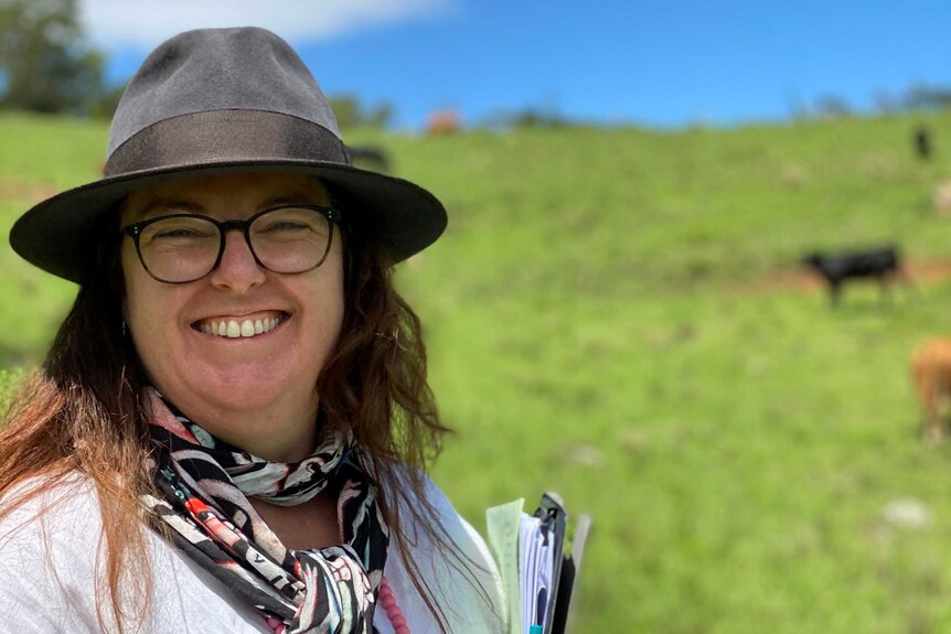 A woman in a field with cows holding a stack of papers