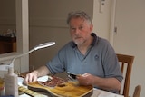 A Caucasian man with a beard, building a guitar at home. 