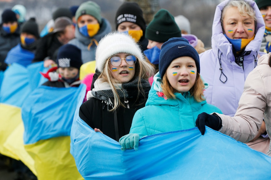 People bundled up in beanies and coats hold a big yellow and blue Ukrainian flag
