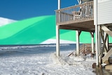 Waves crash underneath a beach-front house for a story about climate risks when buying property.