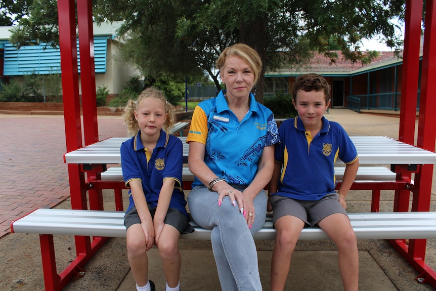A lady with short blonde hair sits between two primary school students.