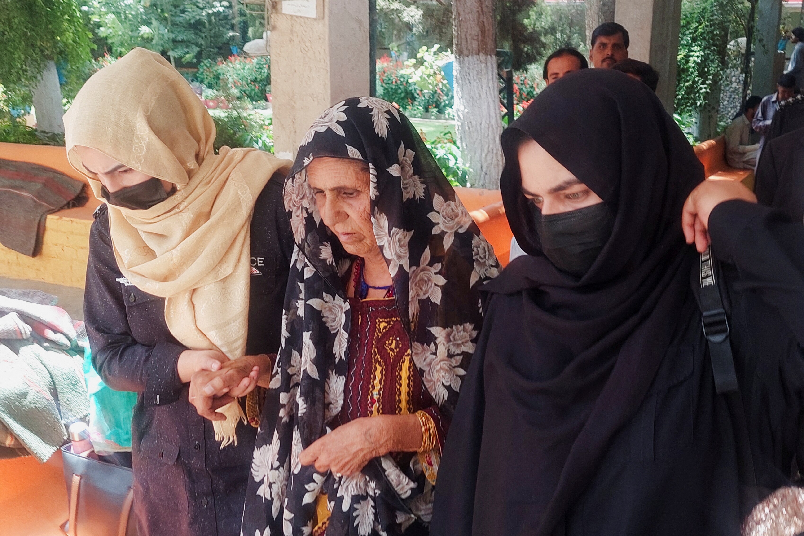 a woman in black and pink floral headscarf is held by two women with headscarves and face obscured and is escorted away.