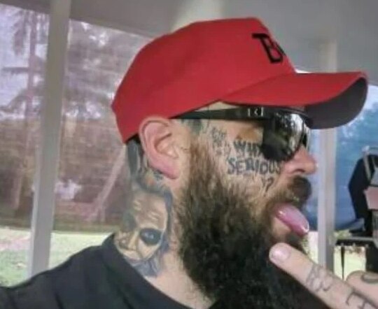 A man in a bright-coloured cap, sporting facial and neck tattoos.