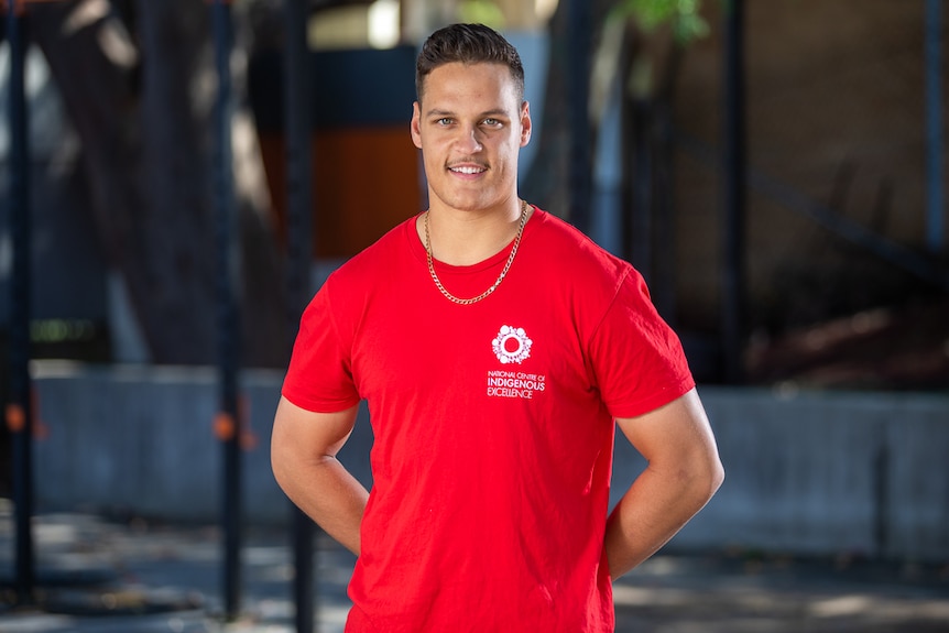 An Aboriginal man wearing a red National Centre of Indigenous Excellence shirt, smiling