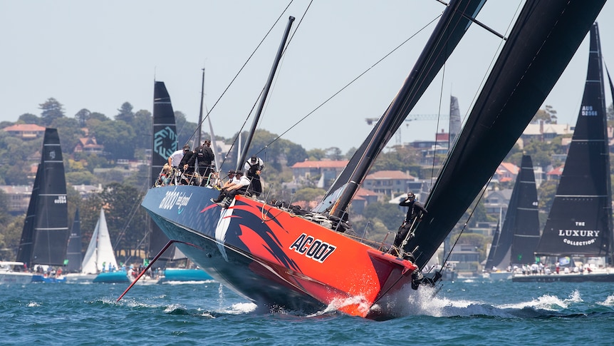 A supermaxi boat races along Sydney Harbour with at least half of the hull lifted out of the water.