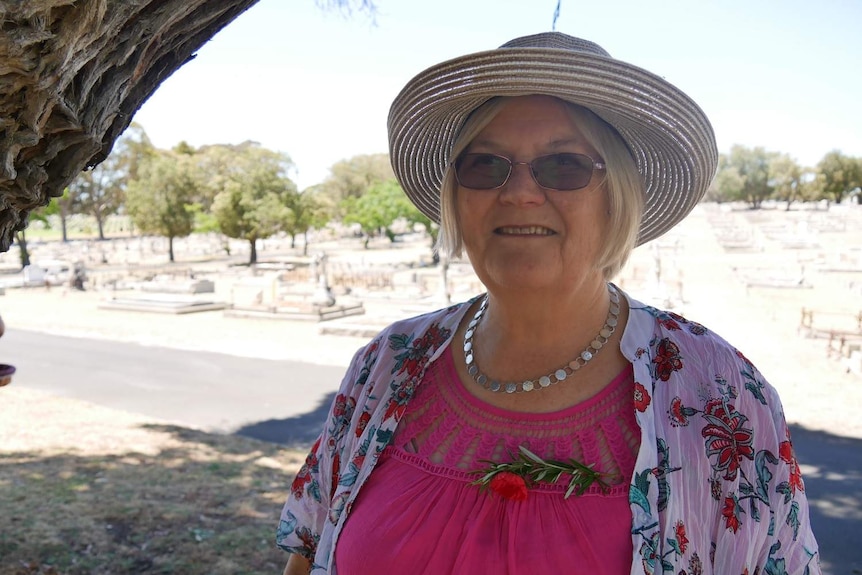 A woman in a hat stands in front of a cemetery