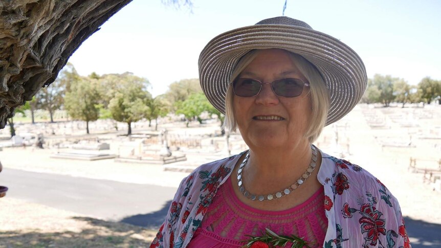 A woman in a hat stands in front of a cemetery