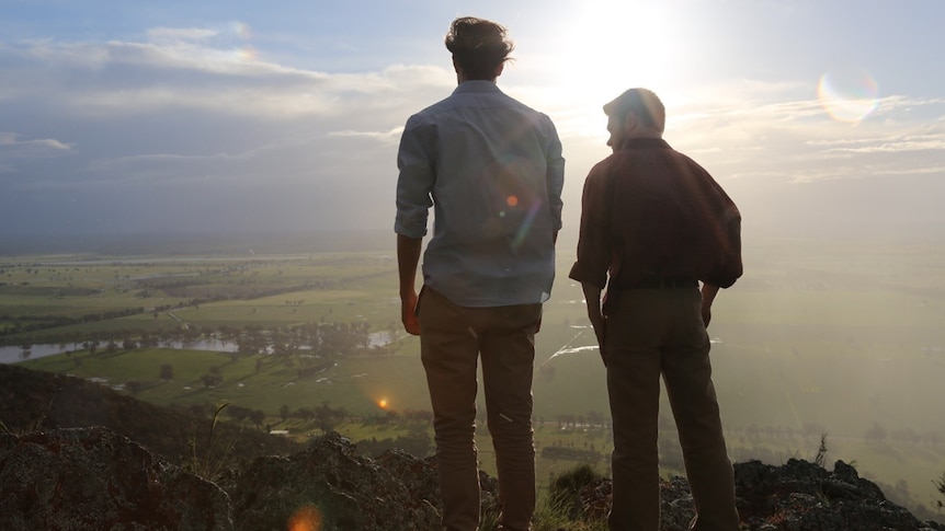 Two men stand on cliff looking out