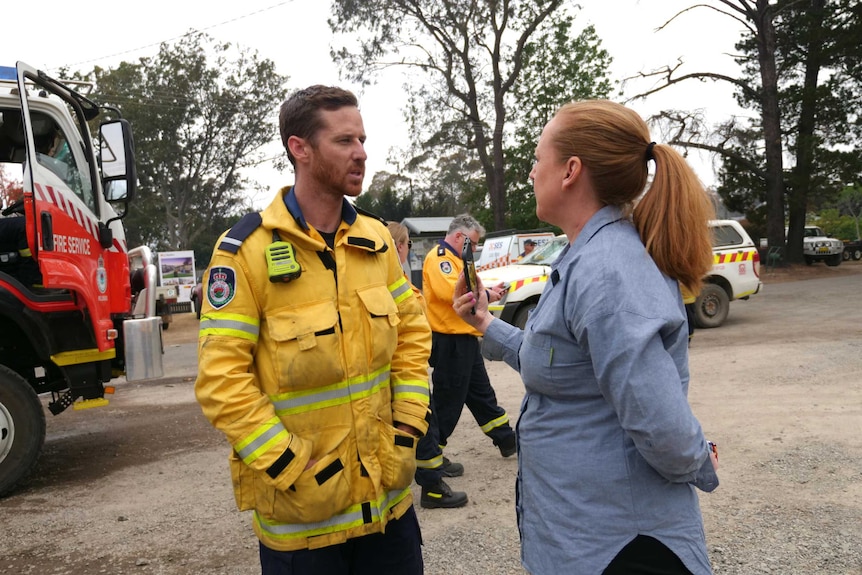 A man in a firefighters uniform talks to a journalist holding up a phone at a fire station.