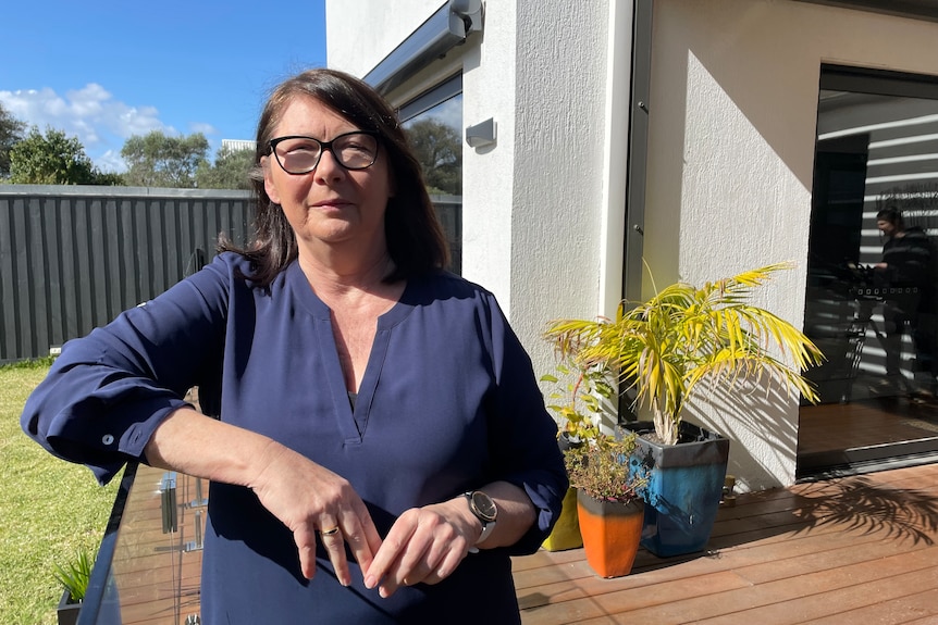 A woman in glasses stands on a house deck.