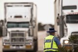 A WA police officer stands with his back to the camera looking at two trucks