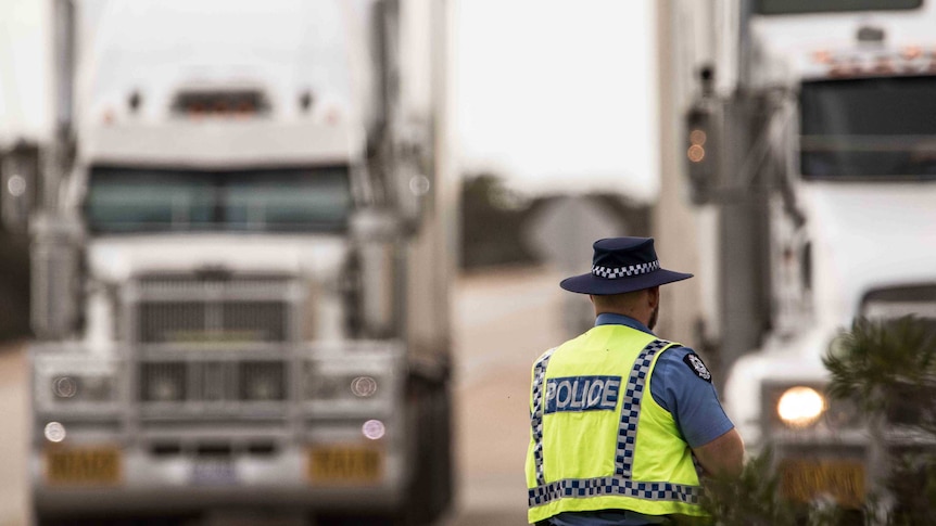 A WA police officer stands with his back to the camera looking at two trucks