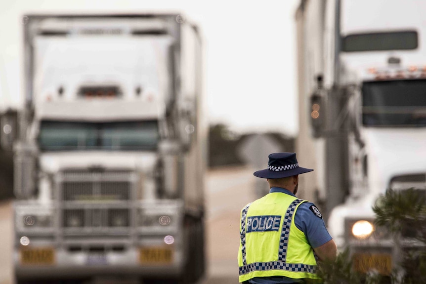 A WA police officer stands with his back to the camera looking at two trucks