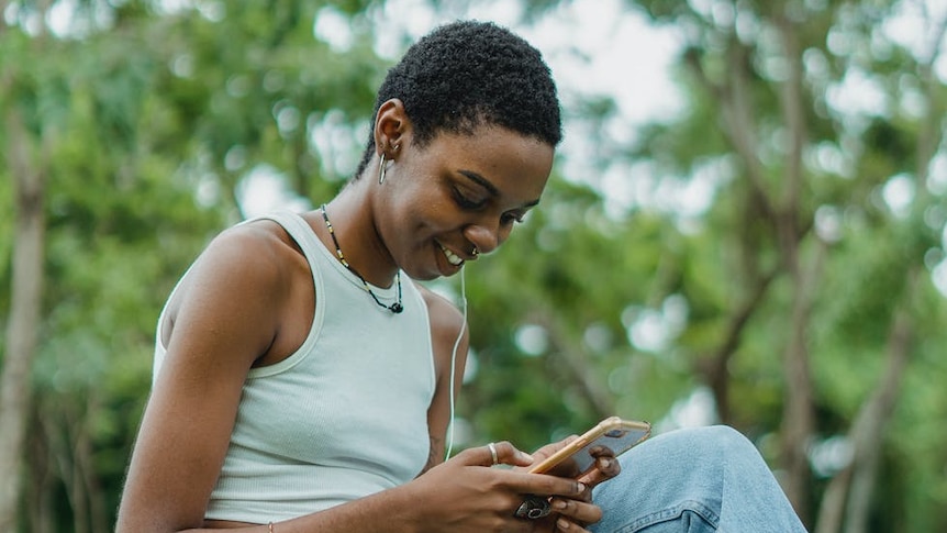 A young woman sits on her phone outside.