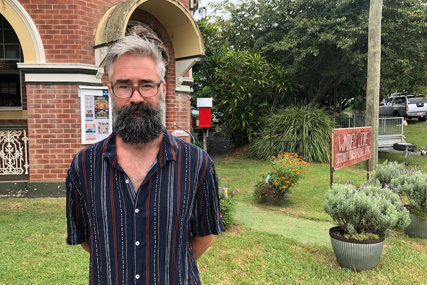A man with a beard and glasses stands outside a building in a garden