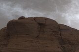 Grey clouds appear above a red, rocky cliff