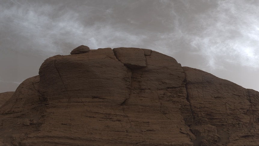Grey clouds appear above a red, rocky cliff