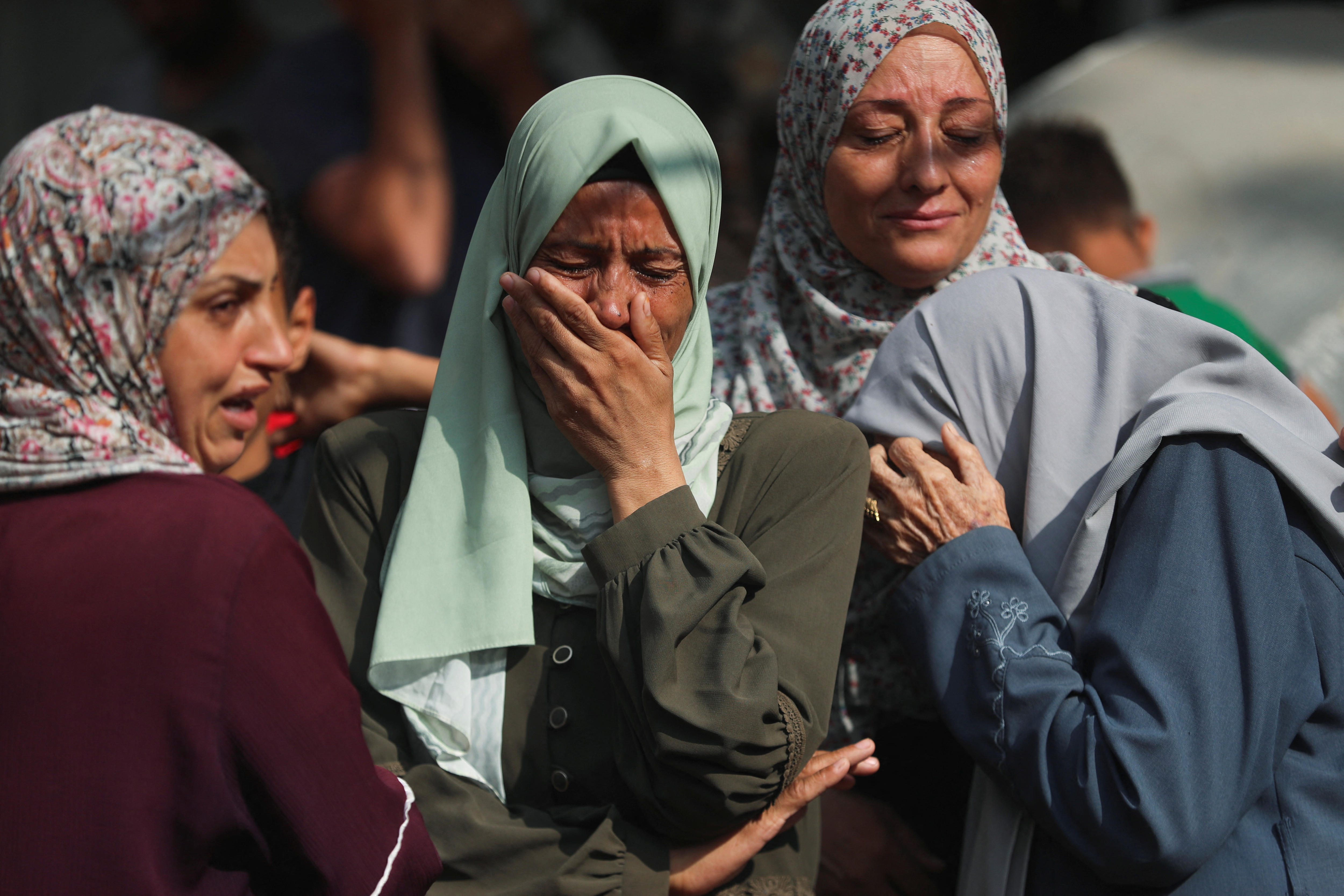 three women wearing head scarves cry and console one another in gaza city