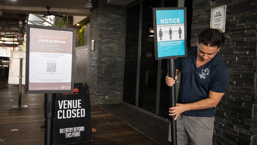 A man positions a social distancing sign, in front of a sign saying venue closed.
