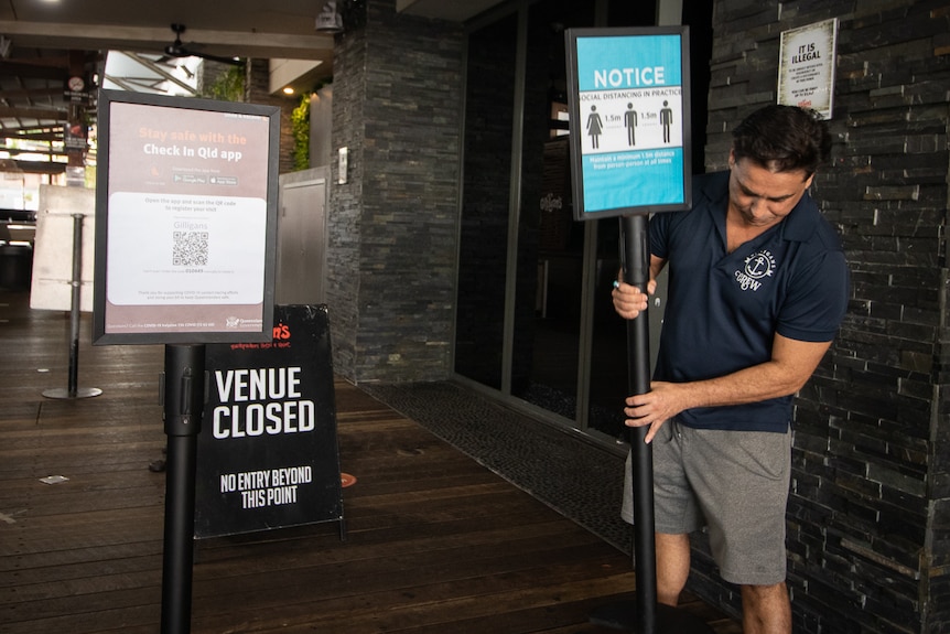 A man positions a social distancing sign, in front of a sign saying venue closed.