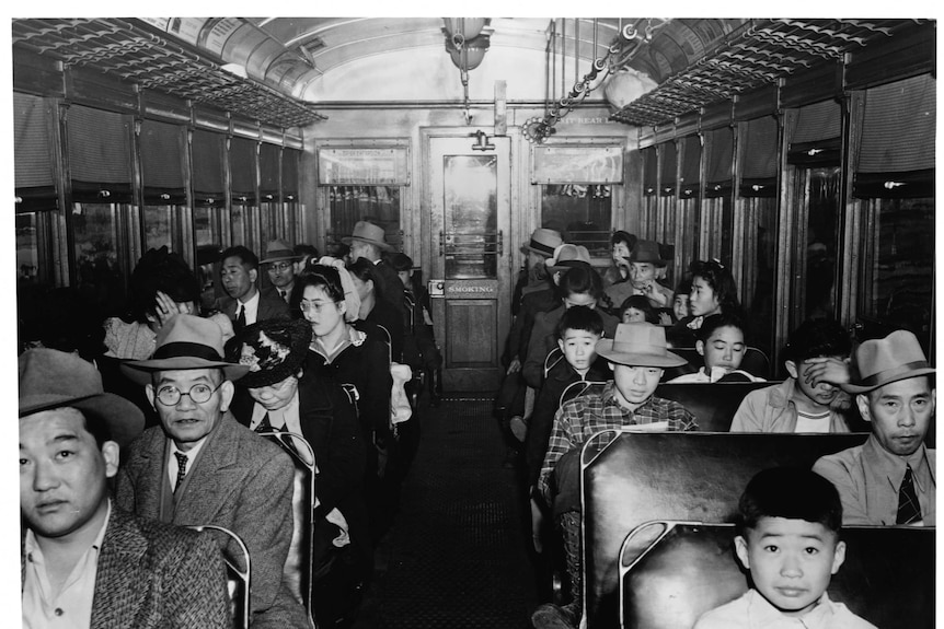 Japanese Americans, young and old, male and female, in an electric train's passenger car.