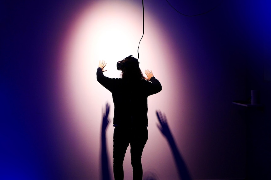 A woman in a room with a VR headset on her face against a white backdrop which is in the spotlight.