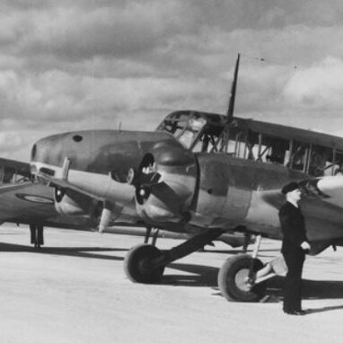 Black & white image of a row aircraft at an airbase with three men in uniform