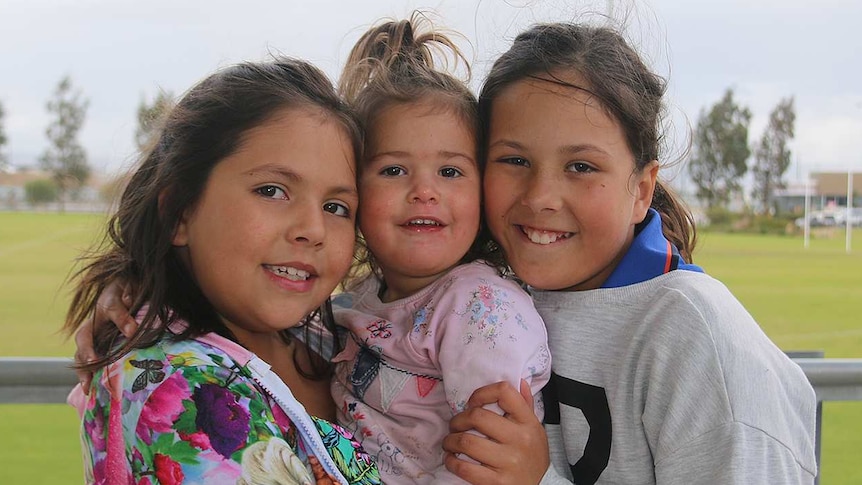 Three sisters hug at a park.