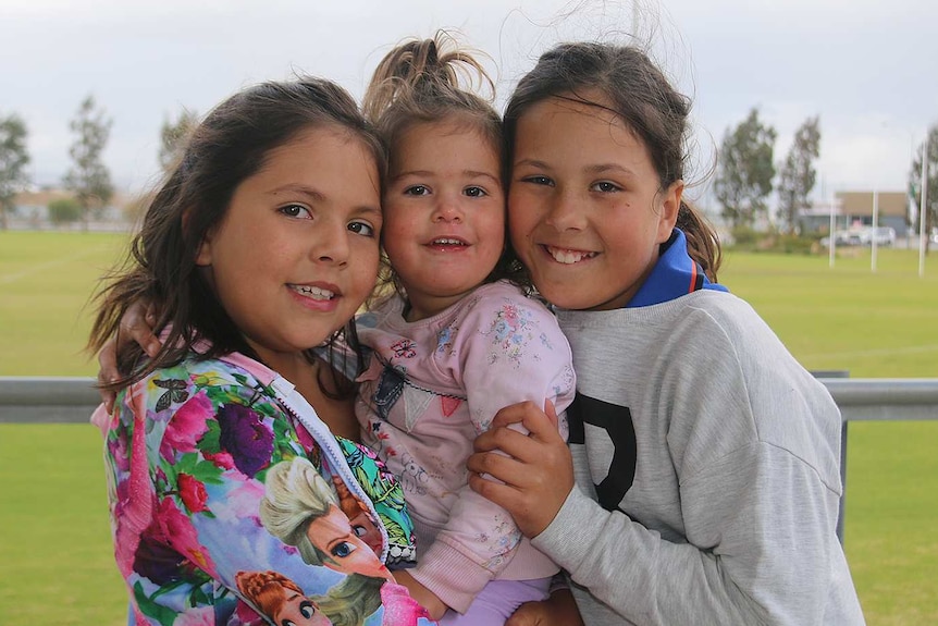 Three sisters hug at a park.