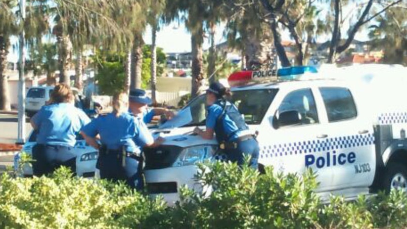 Police gather round bonnet of police car in Mindarie marina as they discuss search for missing fishe