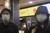 Two people with their faces blurred stand inside a McDonald's restaurant.