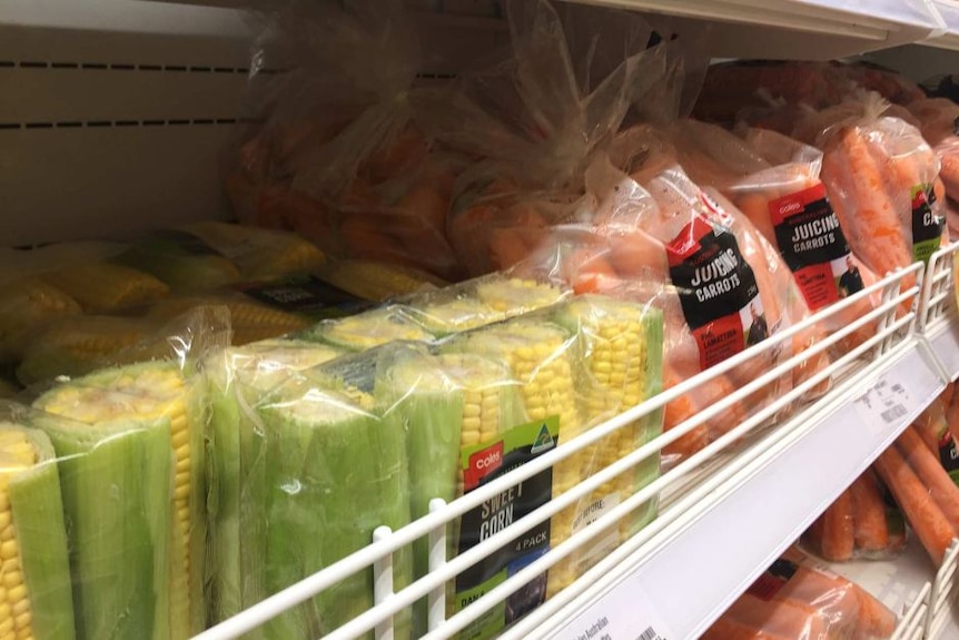 Corn and carrots in plastic packaging sit on a shelf in the supermarket