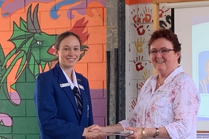 A schoolgirl shakes hands with a teacher in front of a muralled wall.