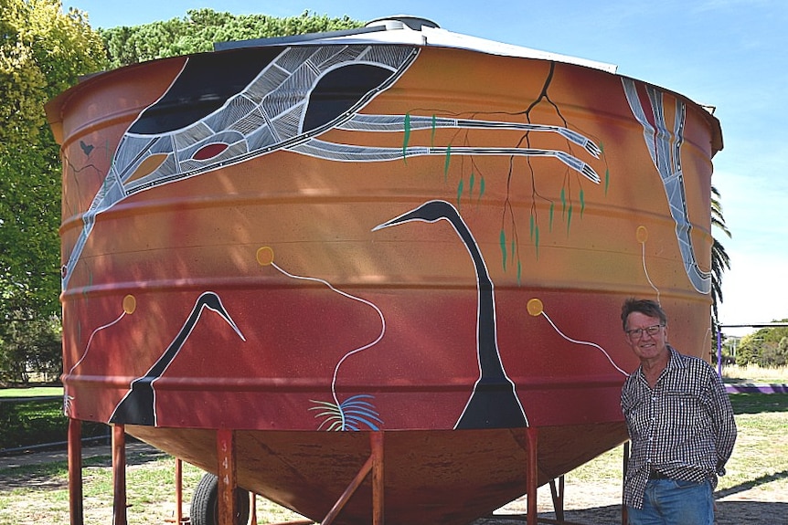 A man is standing in front of a painted grain silo