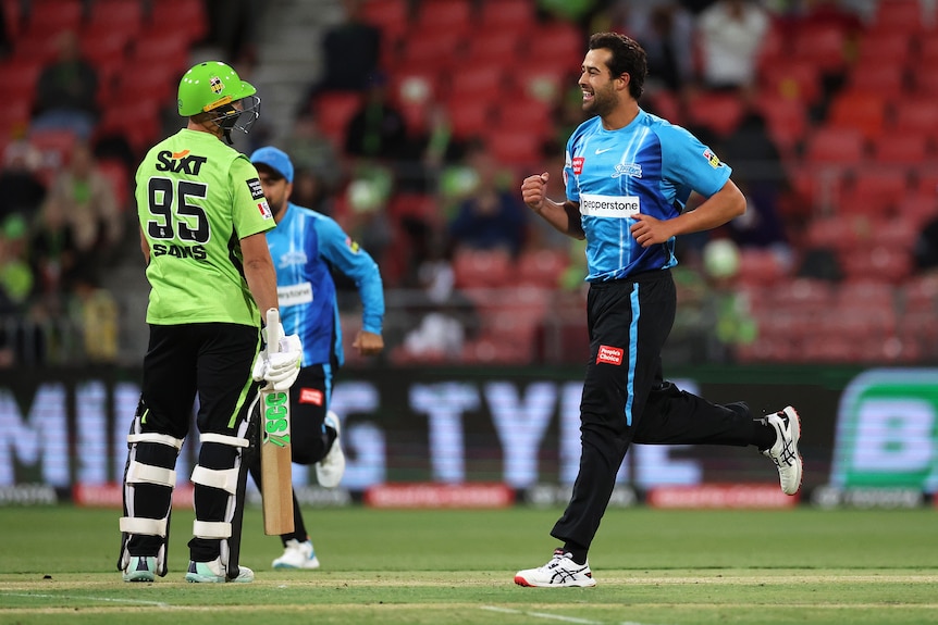 An Adelaide Strikers bowler smiles as he jogs past a dejected Sydney Thunder batsman