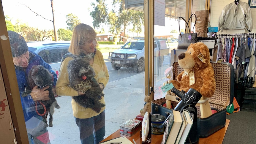 two people holding dogs look into op shop through window