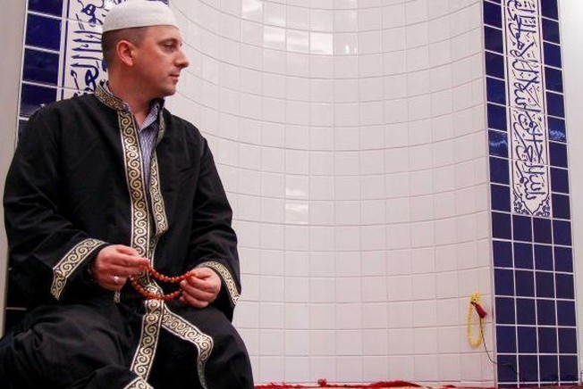 A man wearing Islamic cloth and sitting on the floor