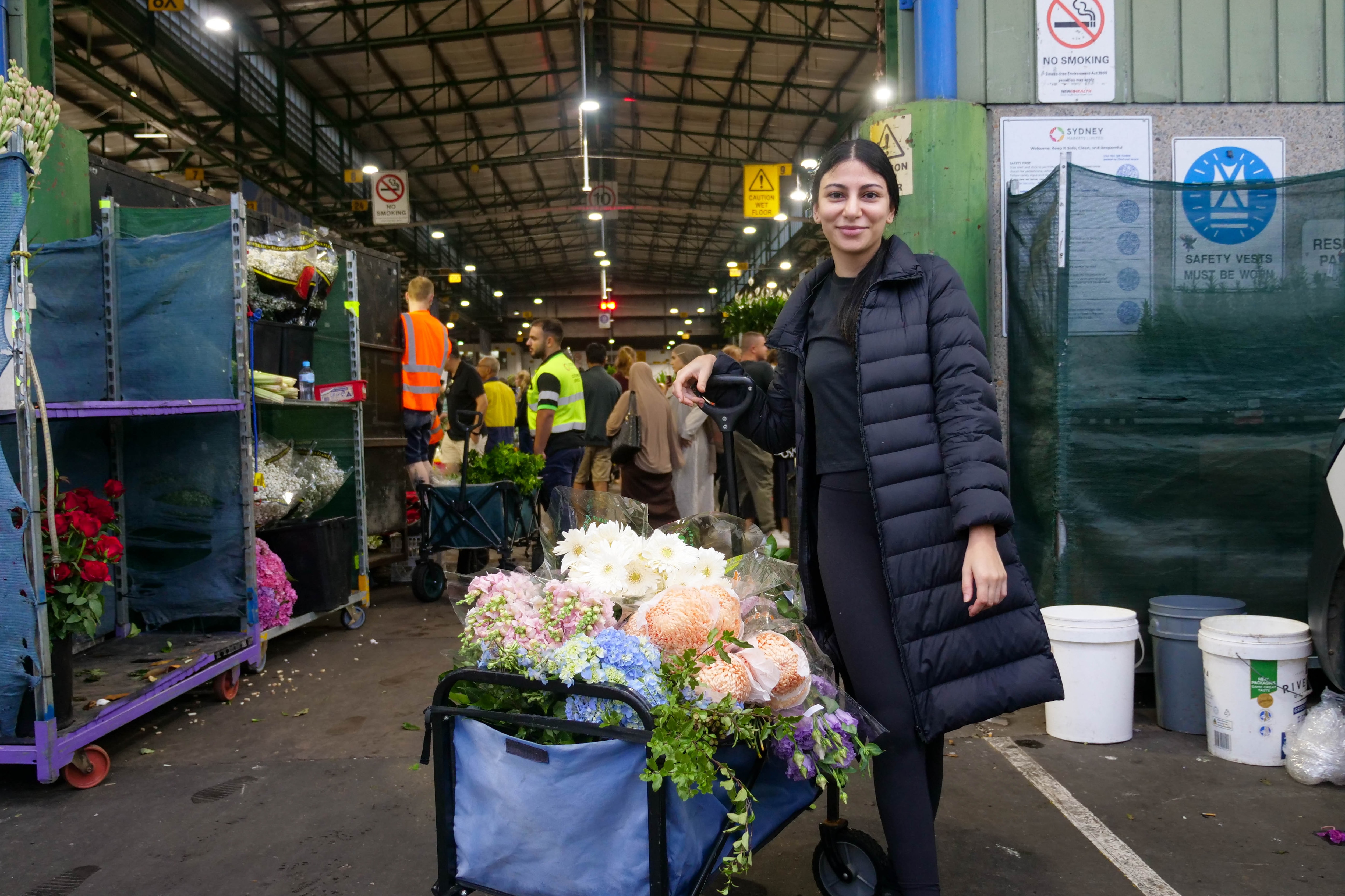 Una mujer con un carro lleno de flores sonríe.