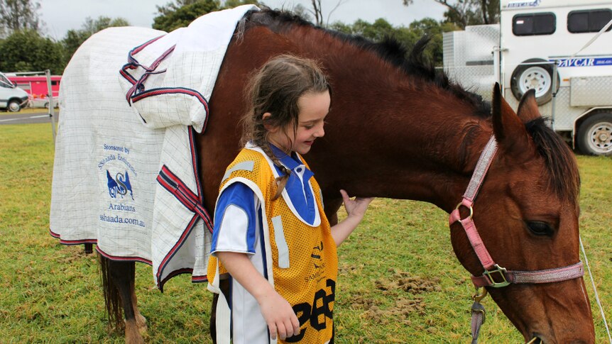 A five-year-old girl patting or tickling under the neck of her pony while she smiles.