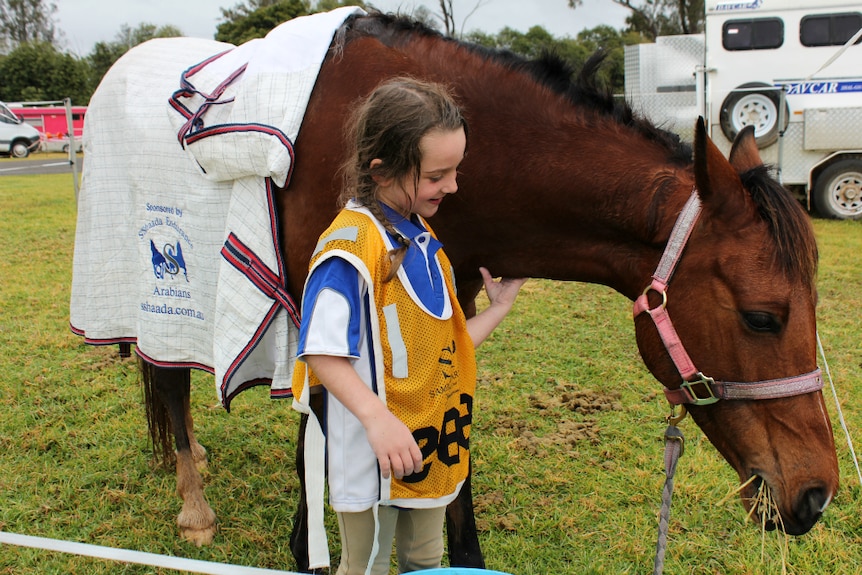 A five-year-old girl patting or tickling under the neck of her pony while she smiles.