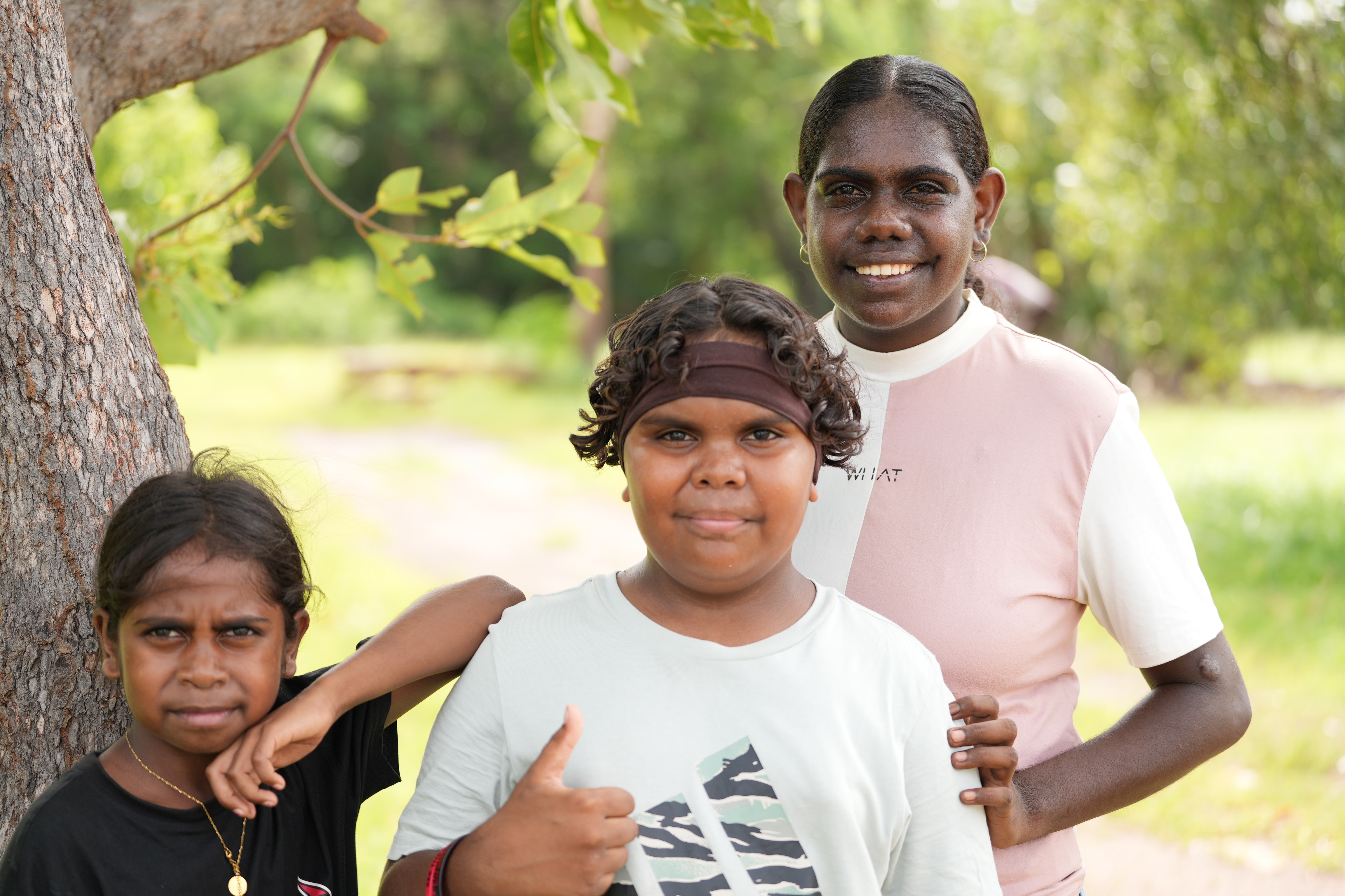Tres personas sonríen mientras están de pie bajo los árboles.