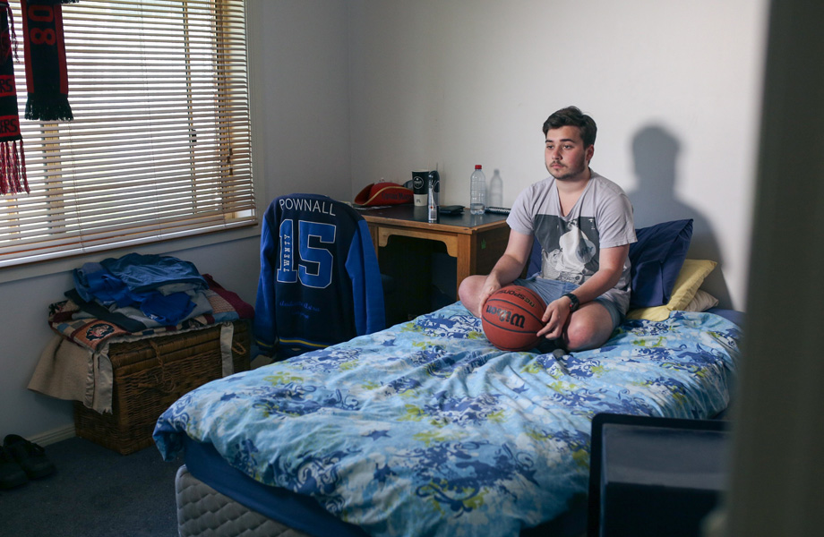 Hamish Pownall sits on his bed holding a basketball. Photo by Margaret Burin.