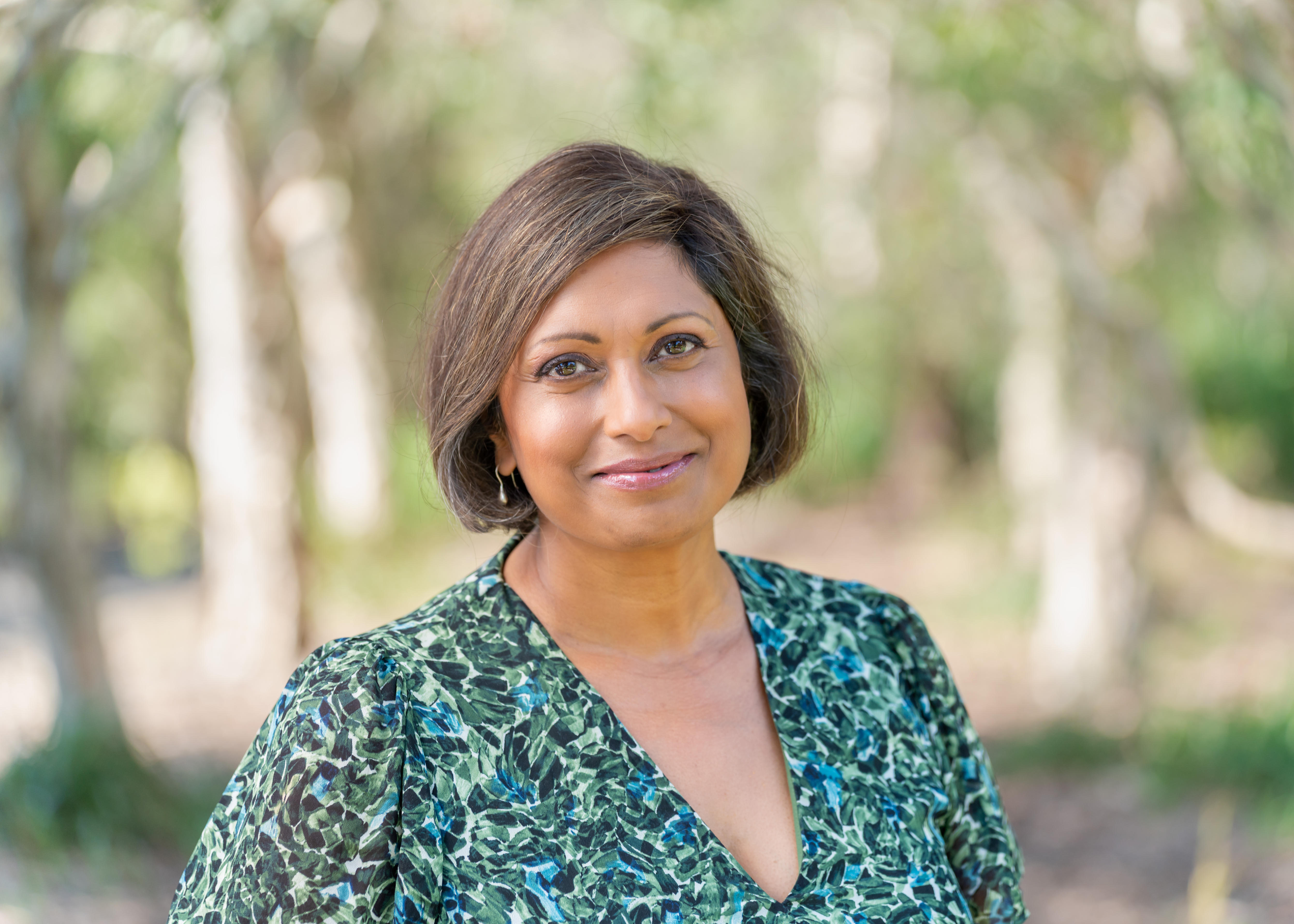 Head shot of a woman wearing a green dress with trees blurred in background.