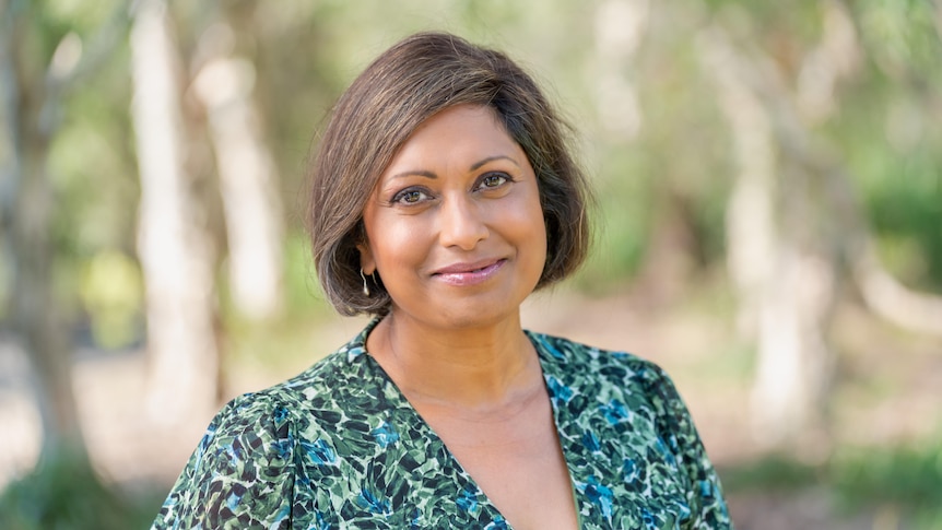 Head shot of a woman wearing a green dress with trees blurred in background.