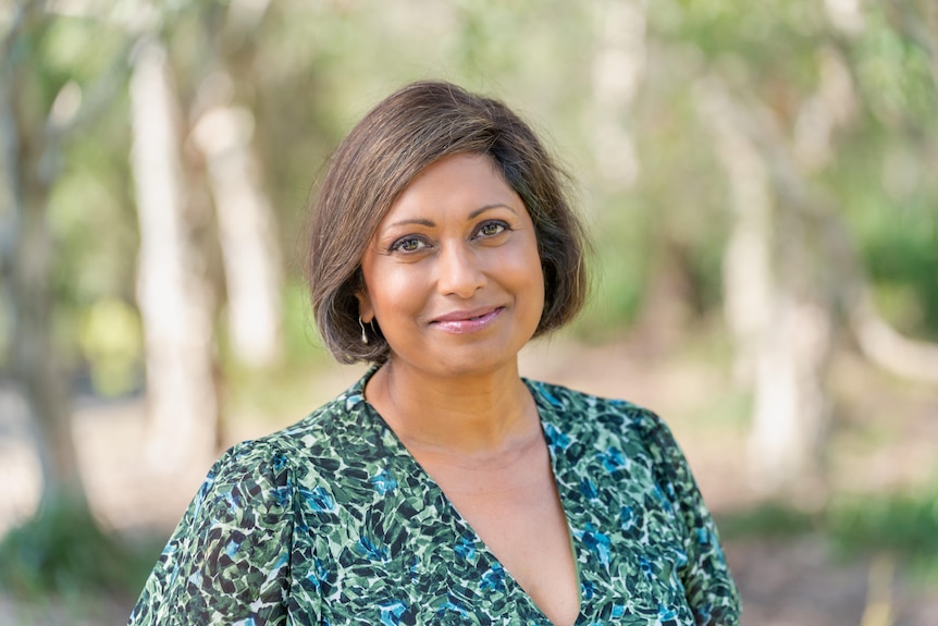 Head shot of a woman wearing a green dress with trees blurred in background.