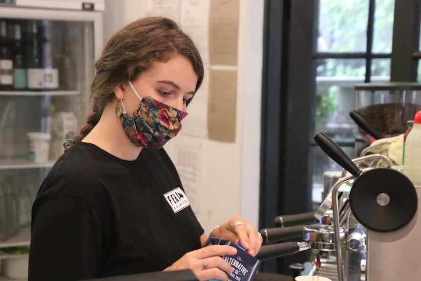 A barista makes coffee wearing a floral face mask in a Perth cafe.